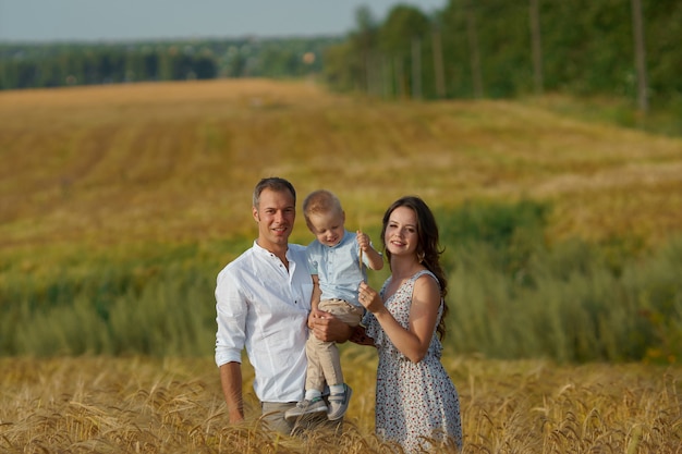 Familia feliz caminando por un campo de trigo. Madre, padre y niño pequeños ocios juntos al aire libre. Los padres y el niño en la pradera de verano.