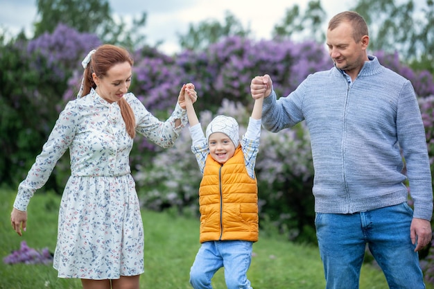 Familia feliz caminando en el hermoso parque. Padres sosteniendo las manos del niño. Mamá, papá y bebé están felices de caminar en el día de verano. Concepto de familia feliz.