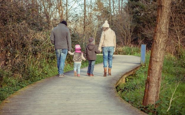 Familia feliz caminando juntos tomados de la mano sobre un camino de madera hacia el bosque