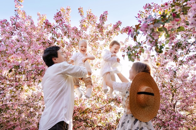 Família feliz caminha no parque no verão no contexto de uma macieira em flor