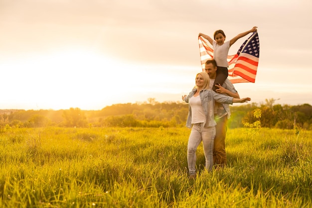 Familia feliz en el campo de trigo con la bandera americana de Estados Unidos en la espalda.