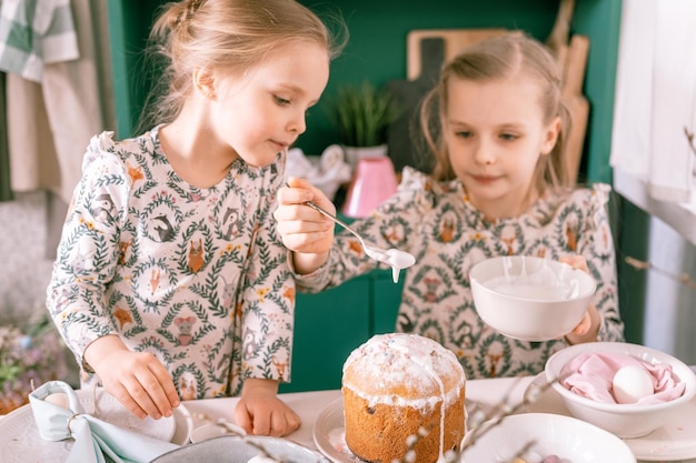 Família feliz cândidas crianças irmãs meninas juntas se divertem prontas férias de páscoa de primavera em casa na mesa de decoração de cozinha e bolos de páscoa padaria glacê doce e doces para almoço ou jantar