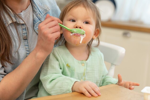 Familia feliz en casa, madre alimentando a su bebé con una cuchara en la cocina, un niño pequeño con