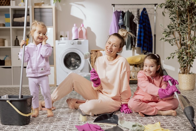 Familia feliz en casa La madre y las hijas limpian la casa Las mujeres jóvenes y los niños aspiran el piso y los limpiadores de trapeador Pequeños ayudantes lindos