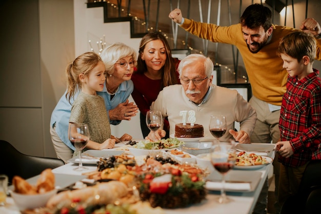 Familia feliz celebrando el cumpleaños del abuelo con pastel y velas en casa