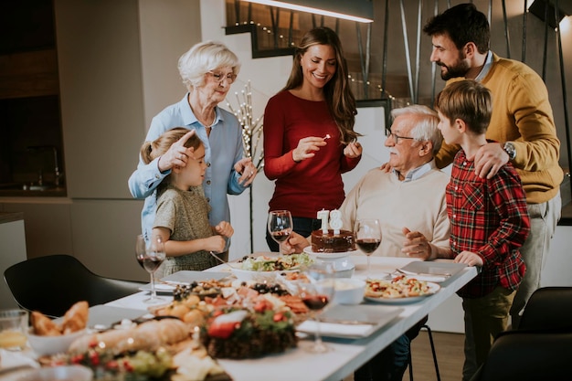 Familia feliz celebrando el cumpleaños del abuelo con pastel y velas en casa