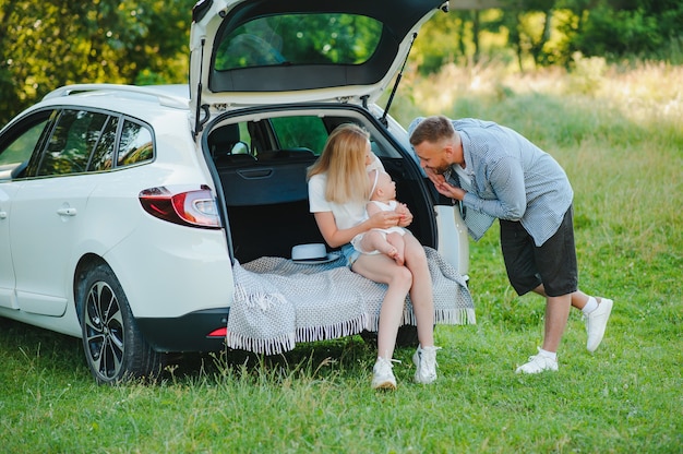 Familia feliz cerca del maletero del coche en un día soleado. Viaje