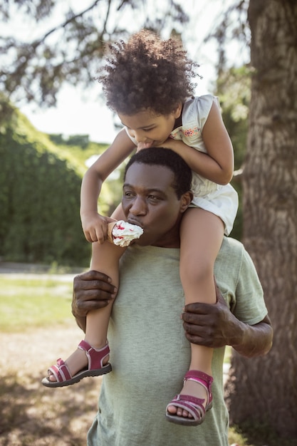 Familia feliz. Chico lindo de piel oscura sentado sobre los hombros de su padre