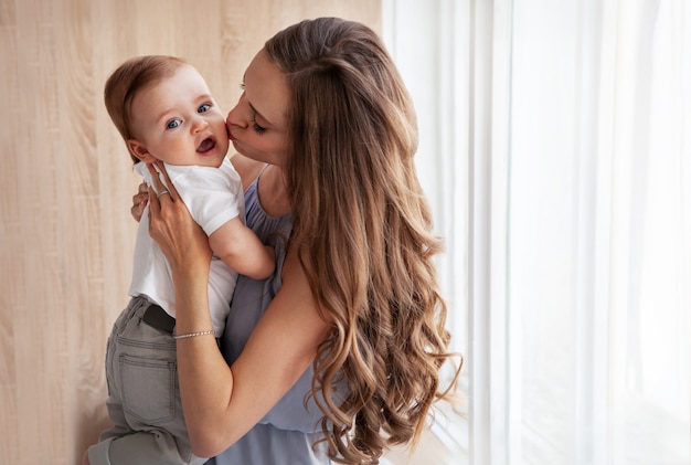 Foto familia feliz. close up retrato de joven atractiva madre sosteniendo al bebé en sus brazos y besando suavemente a su hijo