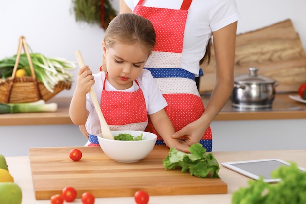 Familia feliz en la cocina Madre e hija cocinando un delicioso desayuno de ensalada fresca Pequeño ayudante cortando y mezclando tomates y vegetación