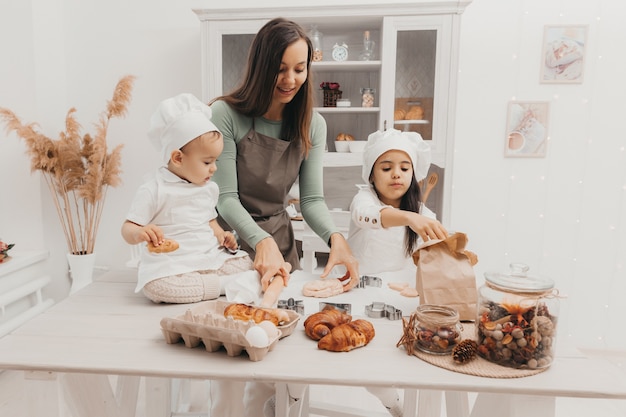 Familia feliz en la cocina. mamá e hijos en trajes de cocinera en la cocina. mamá e hijos preparan masa, hornean galletas