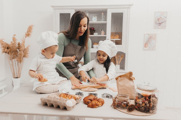 Familia feliz en la cocina. mamá e hijos en trajes de cocinera en la cocina. mamá e hijos preparan masa, hornean galletas