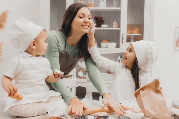 Familia feliz en la cocina. mamá e hijos en trajes de cocinera en la cocina. mamá e hijos preparan masa, hornean galletas