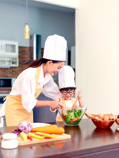 Familia feliz en la cocina. Mamá enseñando a su hijo a cocinar alimentos saludables en las vacaciones de verano.