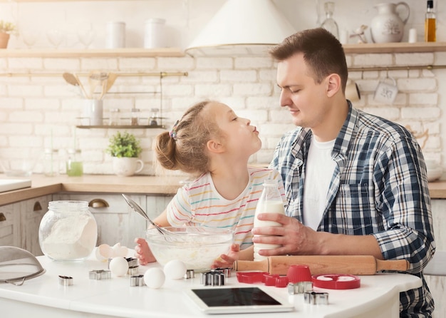 Familia feliz cocinando juntos en la cocina. Linda chica besando a su papá, sonriendo a la cámara