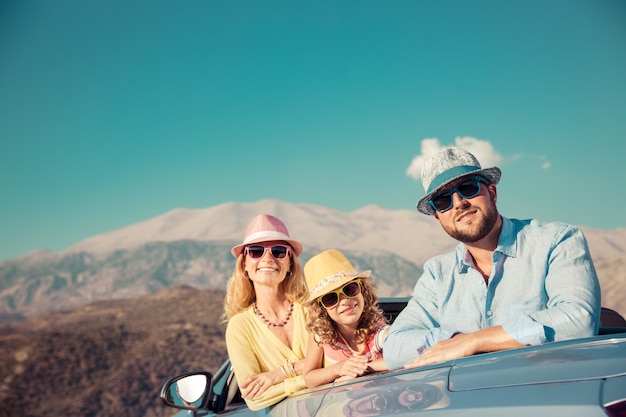 Familia feliz con coloridas gafas de sol y sombreros en su auto convertible con fondo de montañas