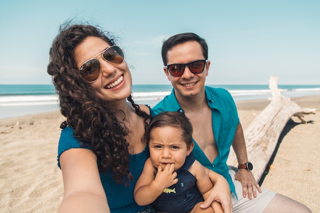 Família feliz com bebê tirando selfie na praia em um dia de verão