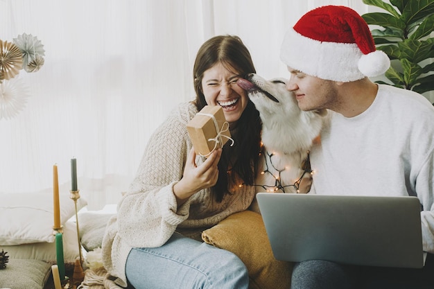 Família feliz com cachorro fofo e laptop trocando presentes de natal comemorando feriados em casa