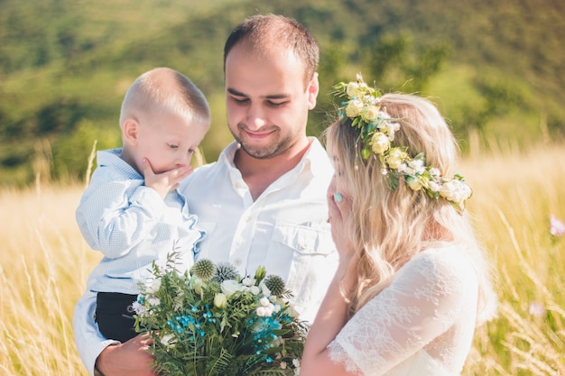 Família feliz com criança caminhando juntos no campo de trigo num dia quente e ensolarado de verão. Foco suave.