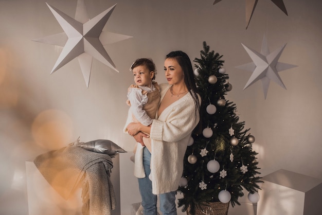 Família feliz com criança comemorando ano novo e natal na árvore de natal decorada e guirlandas