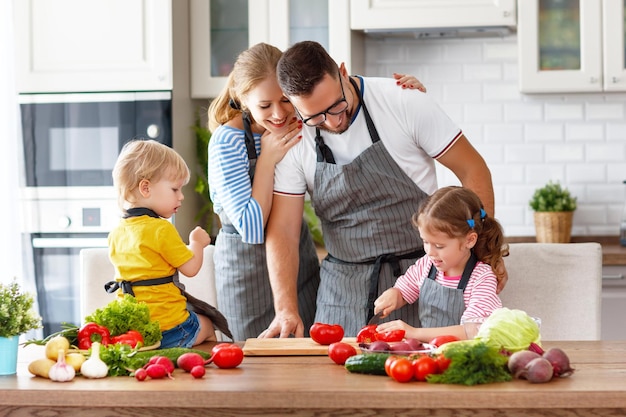 Família feliz com crianças preparando salada de legumes em casa