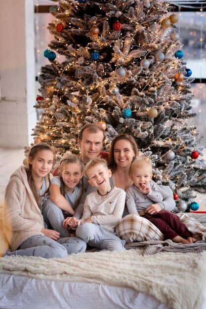 Família feliz com crianças se divertindo e abrindo presentes perto da árvore de Natal.