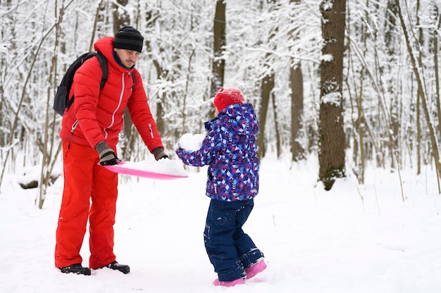 Família feliz com crianças se divertir passando as férias de inverno na floresta de inverno nevado. pai brinca com a filha