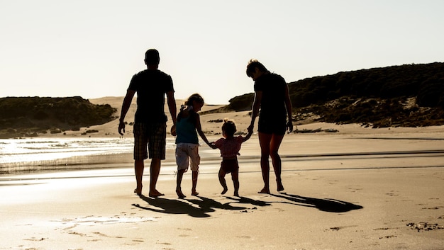 Família feliz com crianças silhueta na praia do mar pôr do sol pai mãe e filhos caminhando na praia