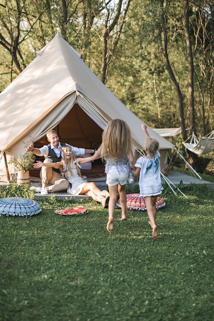 Família feliz, com duas crianças do sexo feminino ao ar livre perto da tenda wigwam tipi em estilo rústico boho