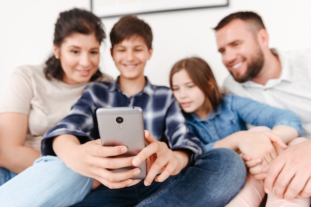 Foto família feliz com duas crianças sentadas no sofá juntas em casa e tirando uma foto de selfie no celular