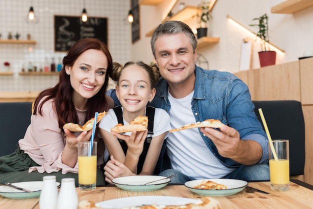 família feliz com filha adolescente comendo pizza no café