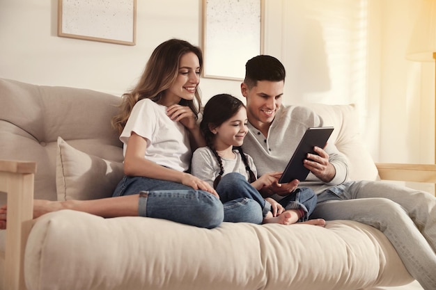 Família feliz com filha pequena usando tablet no sofá na sala de estar