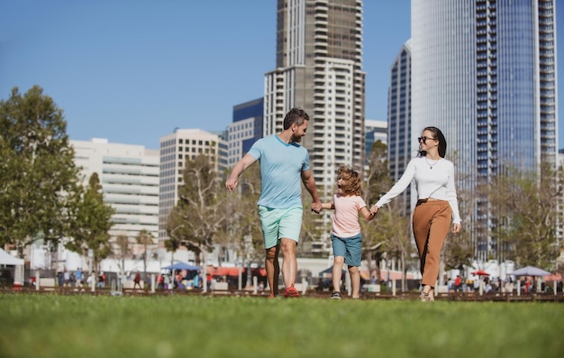 Família feliz com filho pequeno andando pela cidade de mãos dadas