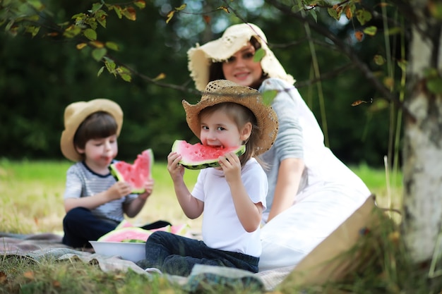 Família feliz com filhos fazendo piquenique no parque, pais com filhos sentados na grama do jardim comendo melancia ao ar livre