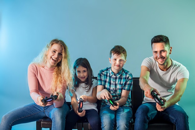 Família feliz com gamepads jogando videogame sobre fundo azul Conceito de entretenimento e jogos em família