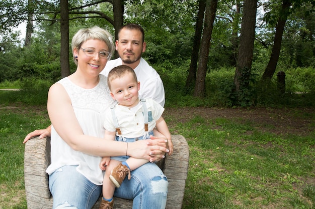 Família feliz com homem, mulher e criança sentada na árvore do banco no parque da cidade. copiar espaço