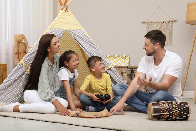 Família feliz com mapa do tesouro perto de brinquedo wigwam em casa