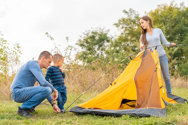 Família feliz com o filho pequeno configurar barraca de acampamento. Infância feliz, viagem de acampamento com os pais.