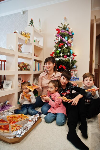 Família feliz com quatro filhos comendo pizza em casa.