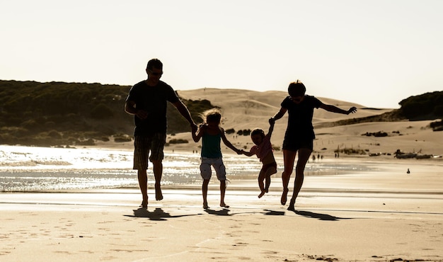 Família feliz com silhueta de crianças no pôr do sol da praia do mar Pai mãe e filhos andando na praia com a luz do sol da tarde