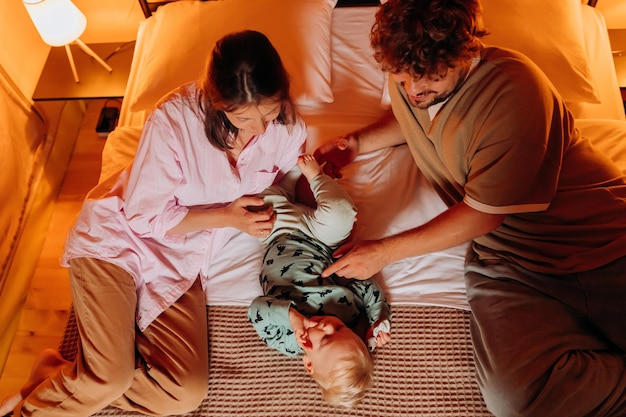 Família feliz com um bebê adorável brincando e passando um tempo juntos em um glamping aconchegante na noite de verão, deitado na cama Barraca de acampamento de luxo para recreação e recreação ao ar livre