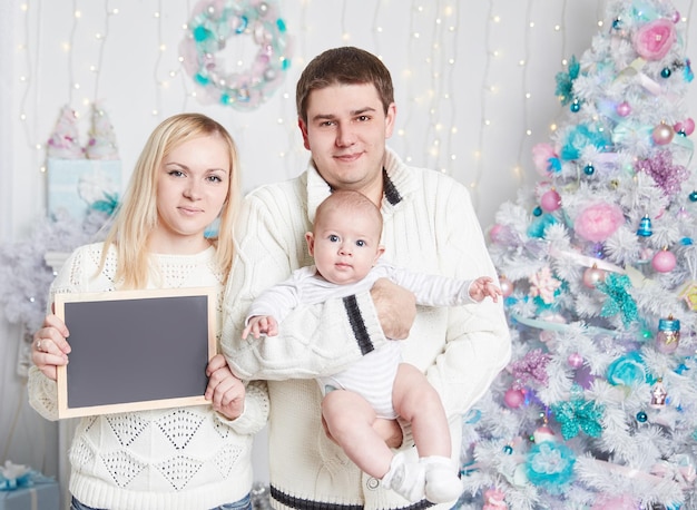 Família feliz com um cartão em branco em pé perto da árvore de Natal