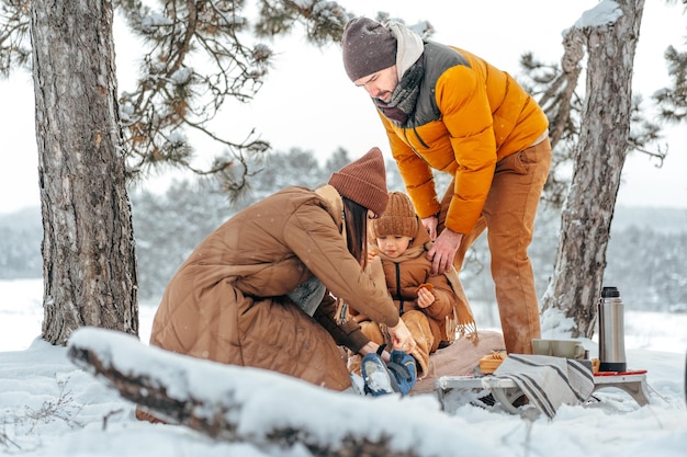 Família feliz com xícaras de chá quente passando tempo juntos na floresta de inverno