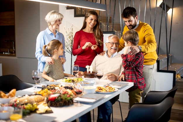 Família feliz comemorando o aniversário do avô com bolo e velas em casa