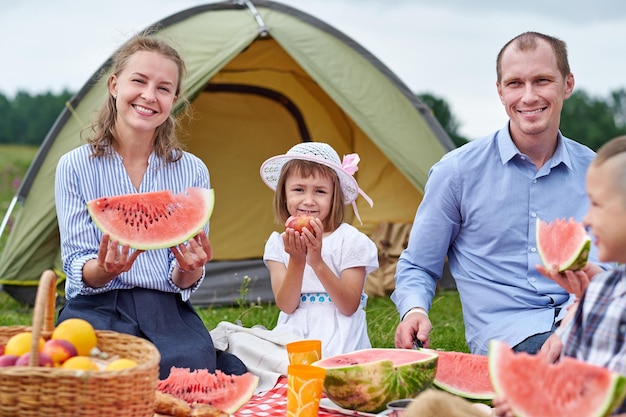 Família feliz comendo melancia no piquenique no prado perto da tenda Mãe pai e filho Desfrutando de férias de acampamento no campo