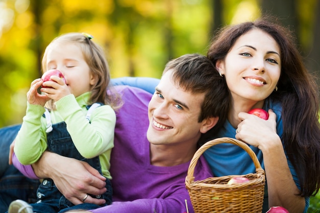 Familia feliz comiendo manzanas en el parque otoño