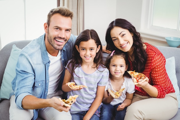 Familia feliz comiendo pizza mientras está sentado en el sofá