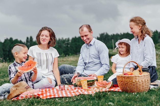 Familia feliz comiendo sandía en un picnic Picnic en el prado o parque Jóvenes amigos y sus hijos en la naturaleza