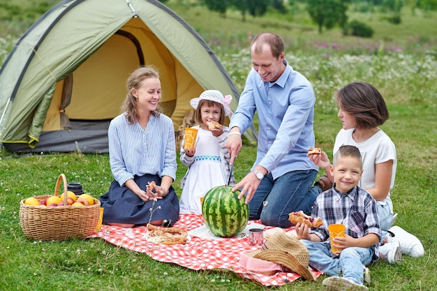 Familia feliz comiendo sandía en un picnic en el prado cerca de la carpa Familia disfrutando de vacaciones de camping en el campo