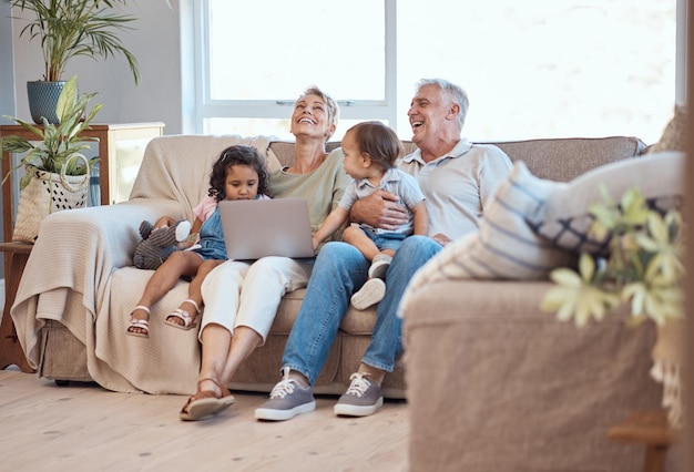 Familia feliz y computadora portátil en el sofá con niños y abuelos en el sofá de casa El hombre y la mujer mayores se relajan en línea con sus nietos adoptados mientras ven películas divertidas o dibujos animados